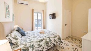 Ein Schlafzimmer mit einem Bett, einem Fernseher, einem Fenster und einer Tür.