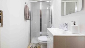 Ein modernes Badezimmer mit einer Duschkabine, einer weißen Toilette und einem Waschtisch mit Spiegel.