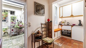 A compact kitchen with a tiled floor, a wooden chair, a small table, and a cabinet with drawers.