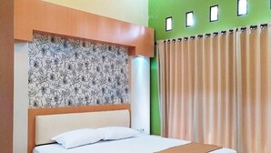 Un lit bien fait dans une chambre dont un mur est peint en vert, avec une tête de lit à motifs et une fenêtre ornée de rideaux.