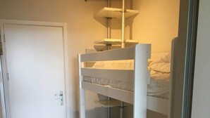 A bunk bed room with a white door, wooden flooring, and a metal shelf unit above the bed.