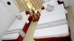 Une chambre d’hôtel avec deux lits simples, une petite table en bois, une lampe et une fenêtre avec des rideaux.