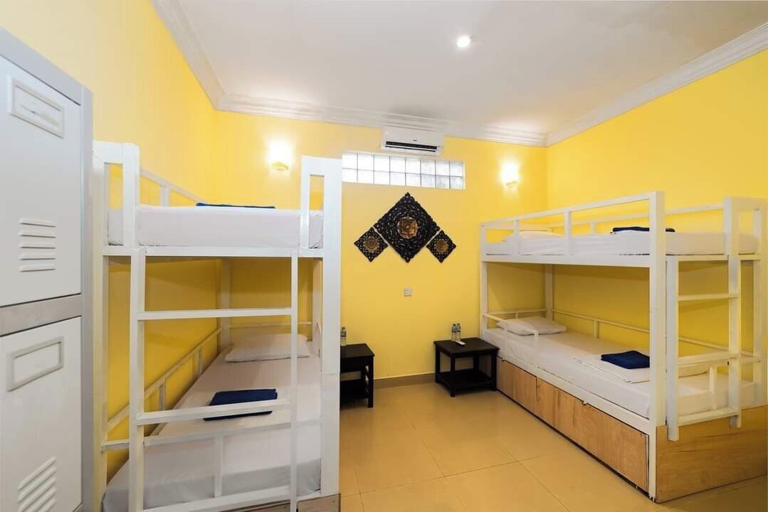 Een slaapzaal met stapelbedden, een kleine tafel en een luchtverkoeler aan de muur.