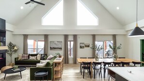 A spacious living area with a high ceiling, large windows, a green sofa, a dining table, and a kitchen area. - Heated Private Pool, Lake view, No steps | Mini Thistle (Hollister)