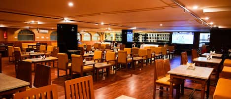 A spacious restaurant with multiple tables and chairs, a bar area, and a television screen.