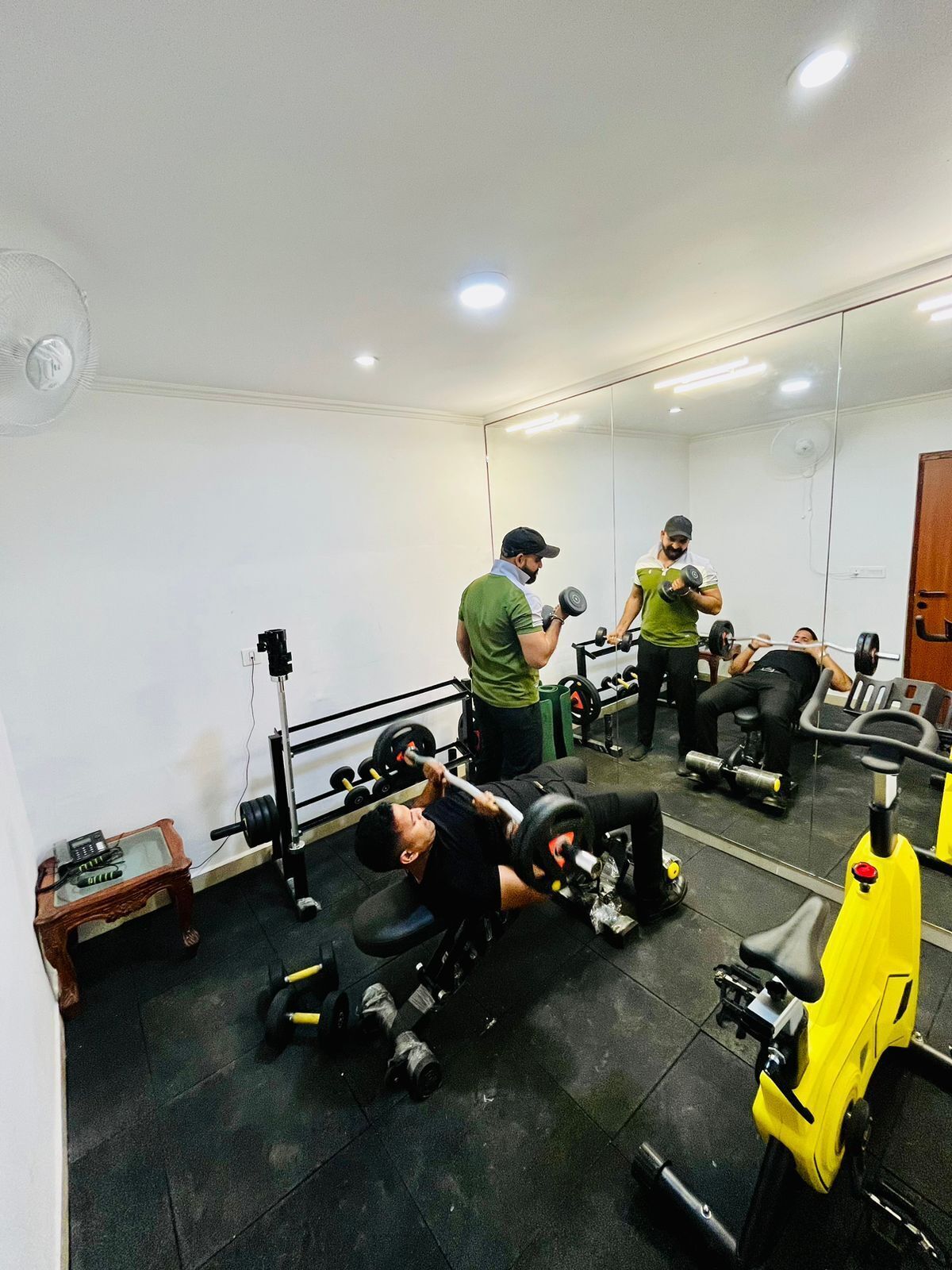 Un gimnasio con diversos equipos de ejercicio, incluyendo mancuernas, una prensa de banca y una bicicleta estática.