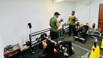 Un gimnasio con diversos equipos de ejercicio, incluyendo mancuernas, una prensa de banca y una bicicleta estática.