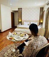 Quarto de hotel com cama, mesas de cabeceira, uma mesa de jantar com café da manhã e uma cadeira de rodas.