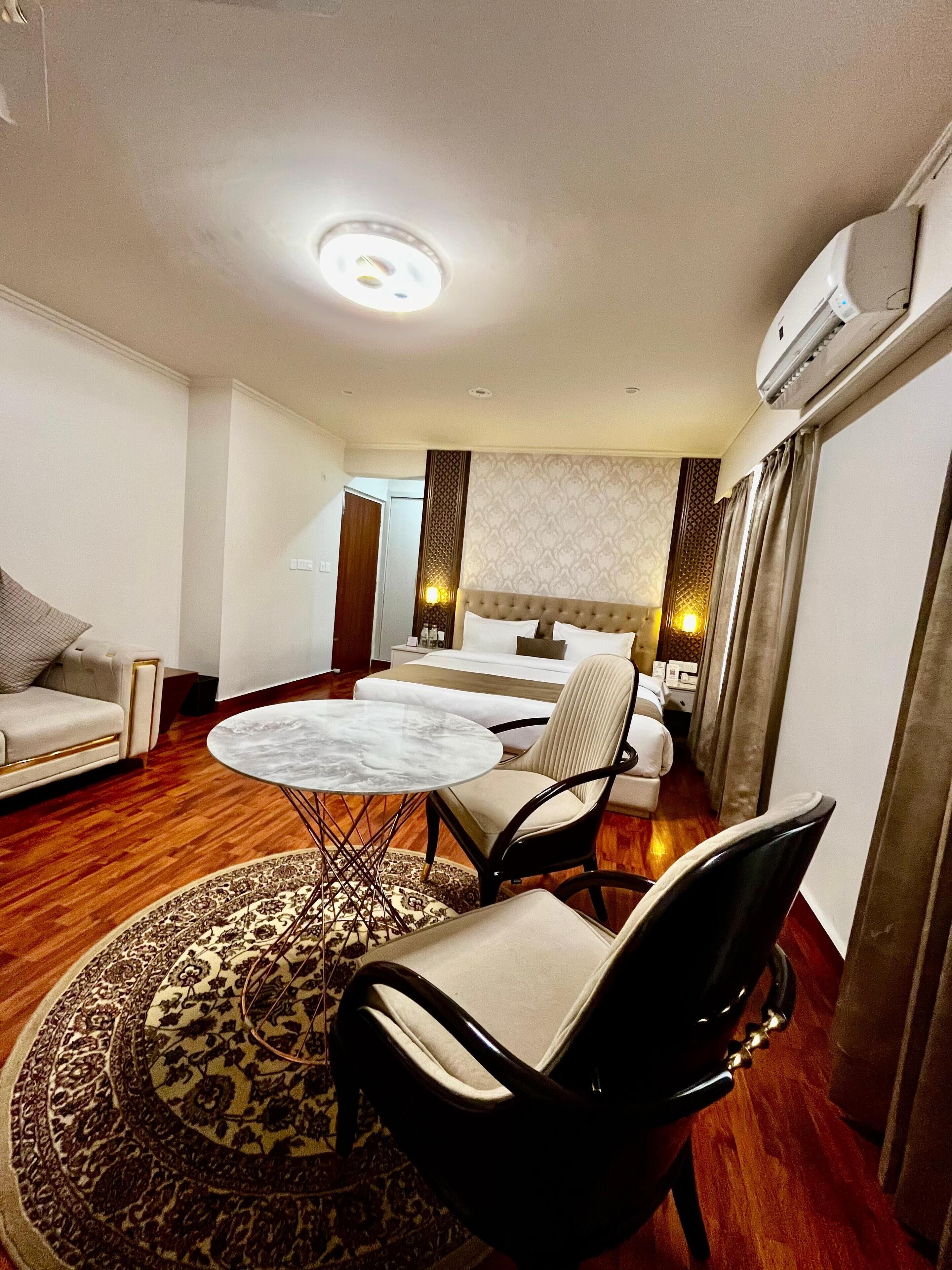 Une chambre d’hôtel comprenant un lit, un coin salon avec une table et des chaises, un canapé, un tapis à motifs et un appareil de climatisation.