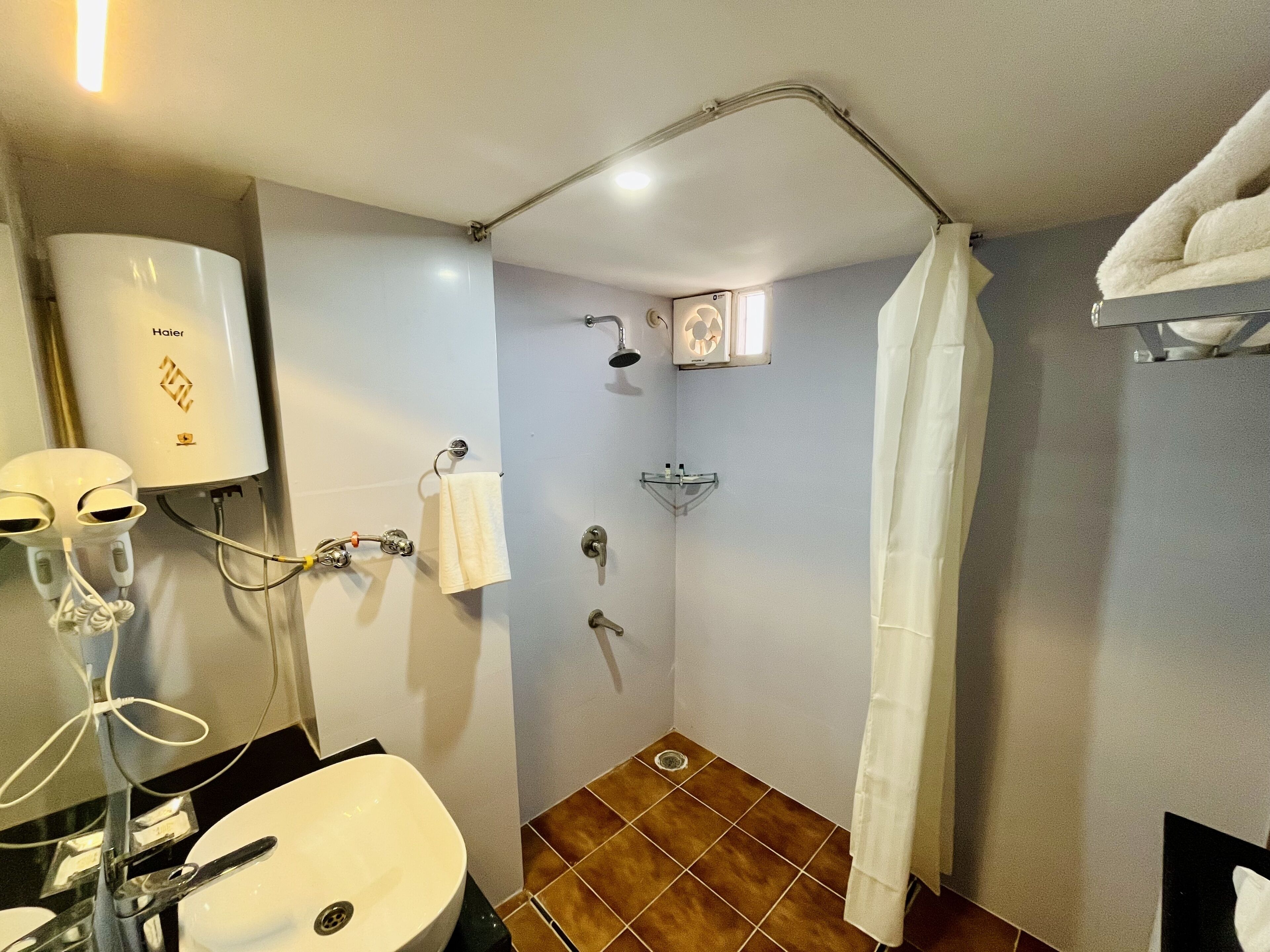 Un baño con un lavamanos blanco, una toalla colgada en la pared, una ducha con repisa de vidrio y una toalla blanca en un perchero.