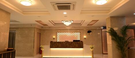 A hotel reception area with a polished floor, a reception desk, a chandelier, and a decorative wall panel.