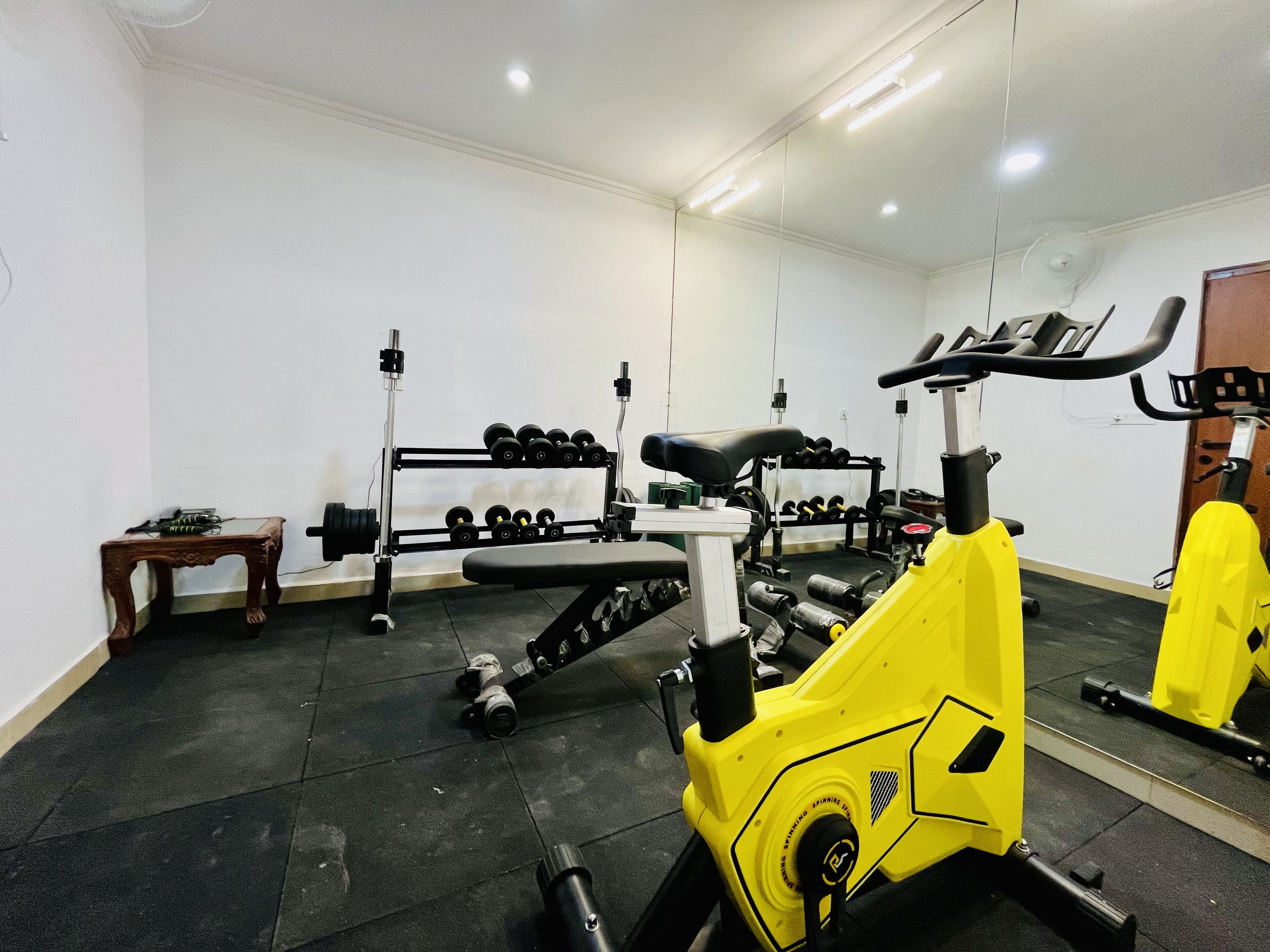 A gym with exercise equipment, including a stationary bike, dumbbells, and a bench.