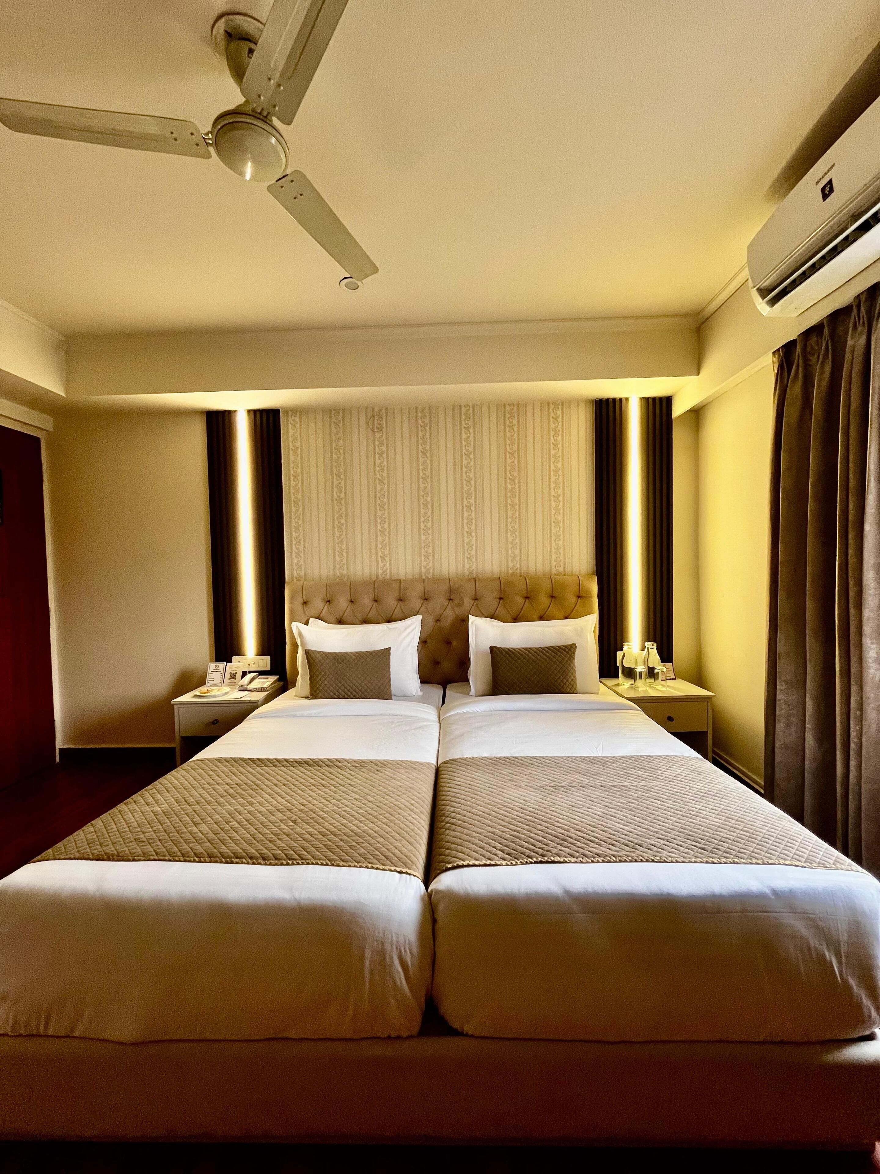 Habitación de hotel con una cama grande, ventilador de techo, mesita de noche con lámpara y aire acondicionado de pared.
