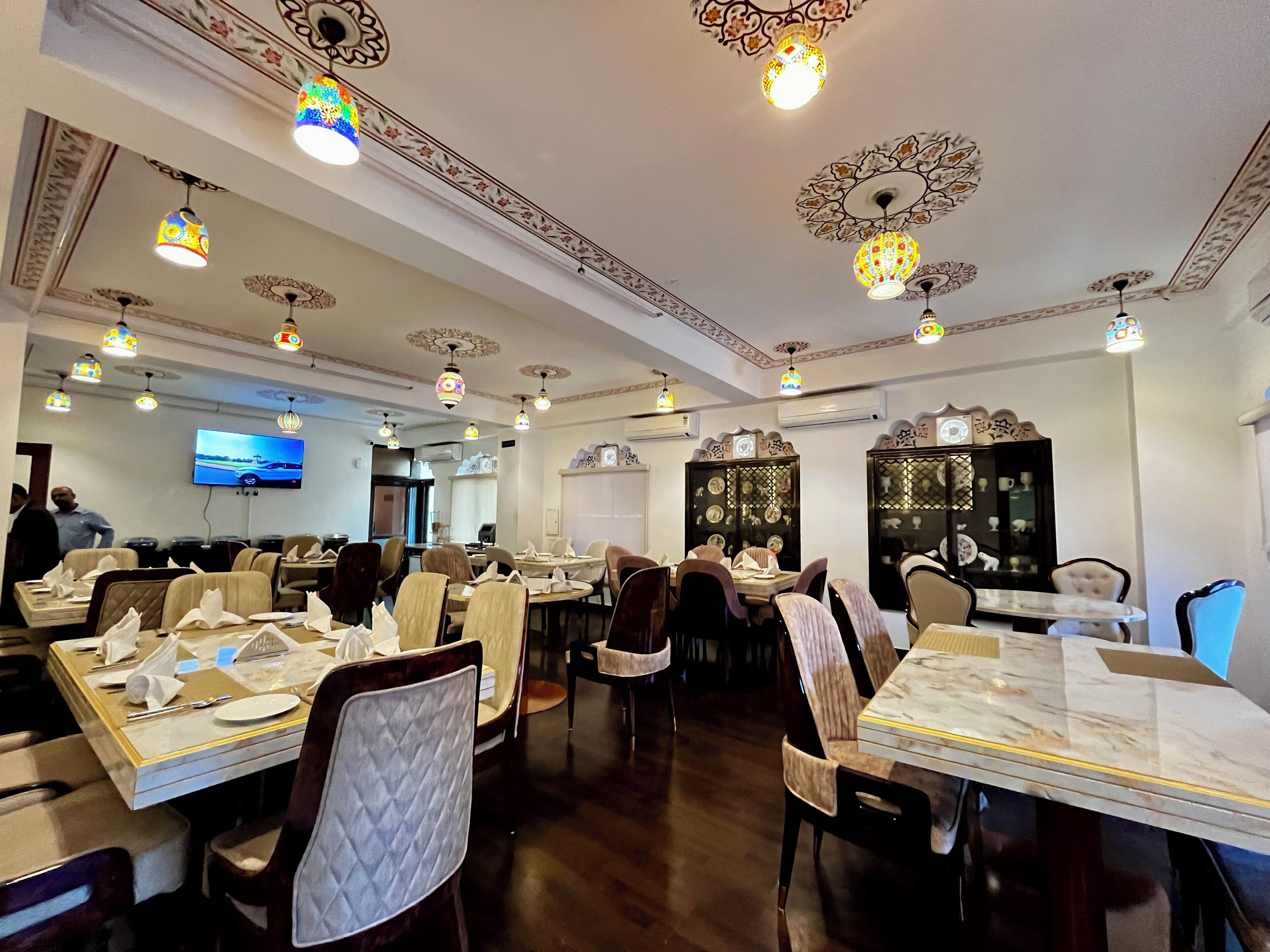 Ein Restaurant mit mehreren Tischen und Stühlen, aufwändigen Deckenverzierungen und einem Fernseher an der Wand.