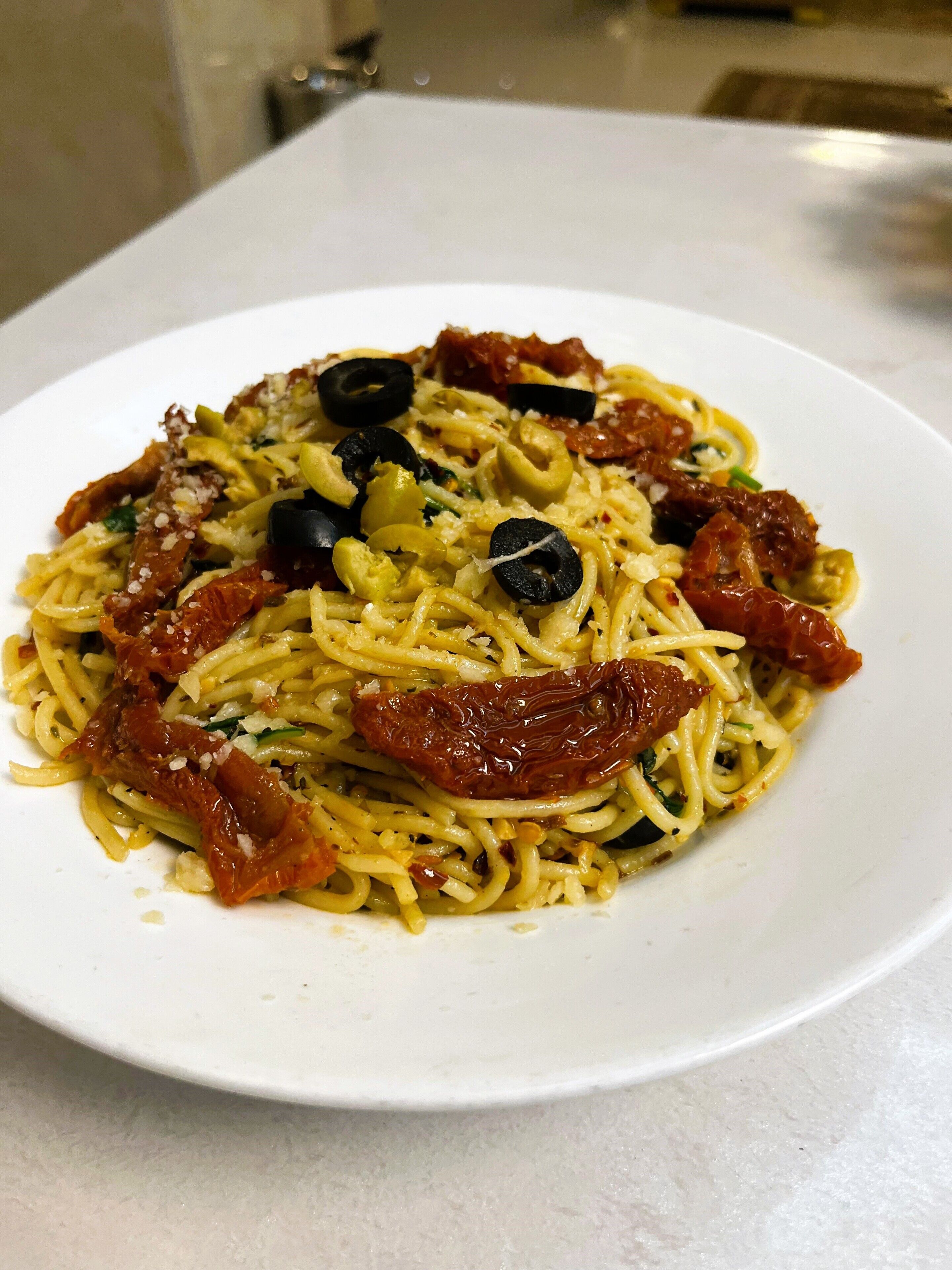 A plate of spaghetti with sun-dried tomatoes, olives, and cheese.