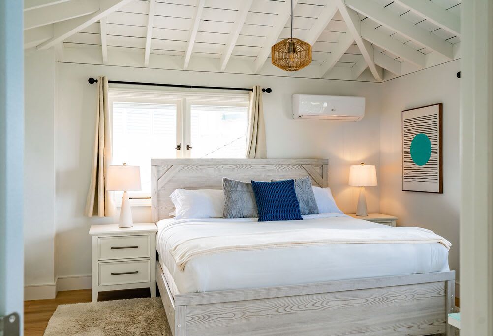 A bedroom with a bed, nightstands, a hanging light, a window with curtains, and an air conditioning unit.