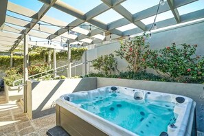 Ein Whirlpool unter einer Pergola mit freiem Blick auf den umliegenden Garten und einer Betonmauer.