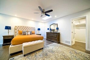 Ein Schlafzimmer mit einem großen Bett, einem Deckenventilator, einem Schminktisch, einem Spiegel und einem begehbaren Kleiderschrank.