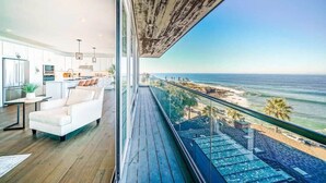Ein modernes Wohnzimmer mit einem weißen Sofa, einem Esstisch und Blick auf den Ozean und den Strand durch große Fenster.