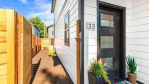 A white building with the number 133 on the door, a wooden fence, and potted plants outside.
