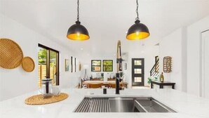 A modern kitchen with white countertops, a stainless steel sink, and two black pendant lights.