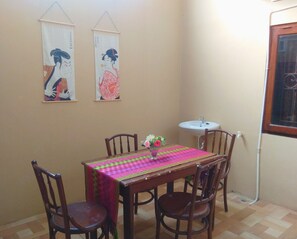 A dining area with a table covered by a colorful tablecloth, surrounded by wooden chairs. Two wall-mounted scrolls are visible above the table. - Pesona Mentari Homestay by FH Stay (Ngaglik)