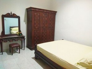 A bedroom with a wooden wardrobe, a bedside table with a mirror, and a bed with a white mattress. - Pesona Mentari Homestay by FH Stay (Ngaglik)