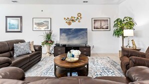 A living room with a sofa set, a coffee table, a TV, and decorative items. - Spacious 10BR resort home with private pool, game room, and room for 25. (Kissimmee)