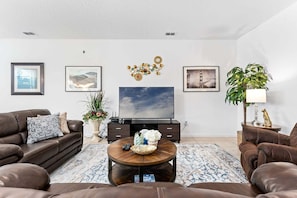 A living room with a sofa set, a coffee table, a TV, and decorative items. - Spacious 10BR resort home with private pool, game room, and room for 25. (Kissimmee)