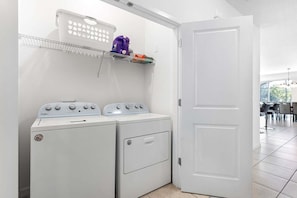 Lavandería con dos lavadoras y secadoras Whirlpool, una puerta blanca y un estante con un calentador de agua púrpura y otros objetos.
