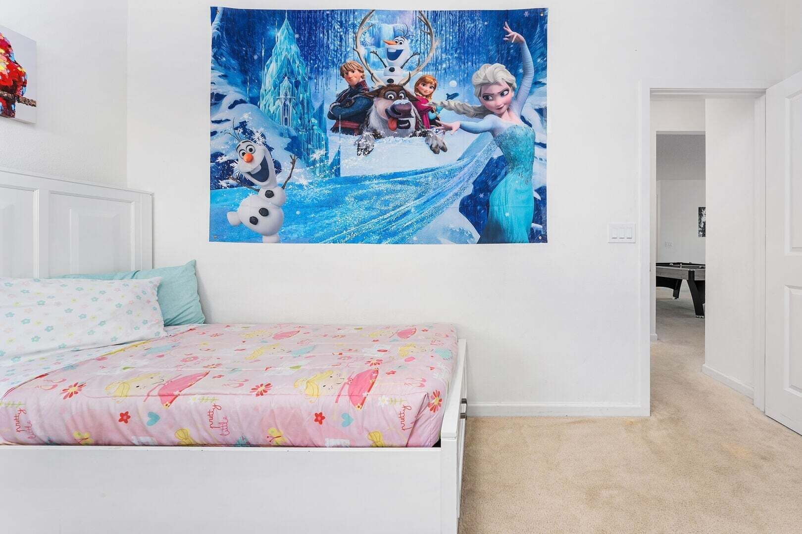 A bedroom with a bed, a wall with a movie poster, and a door leading to another room.