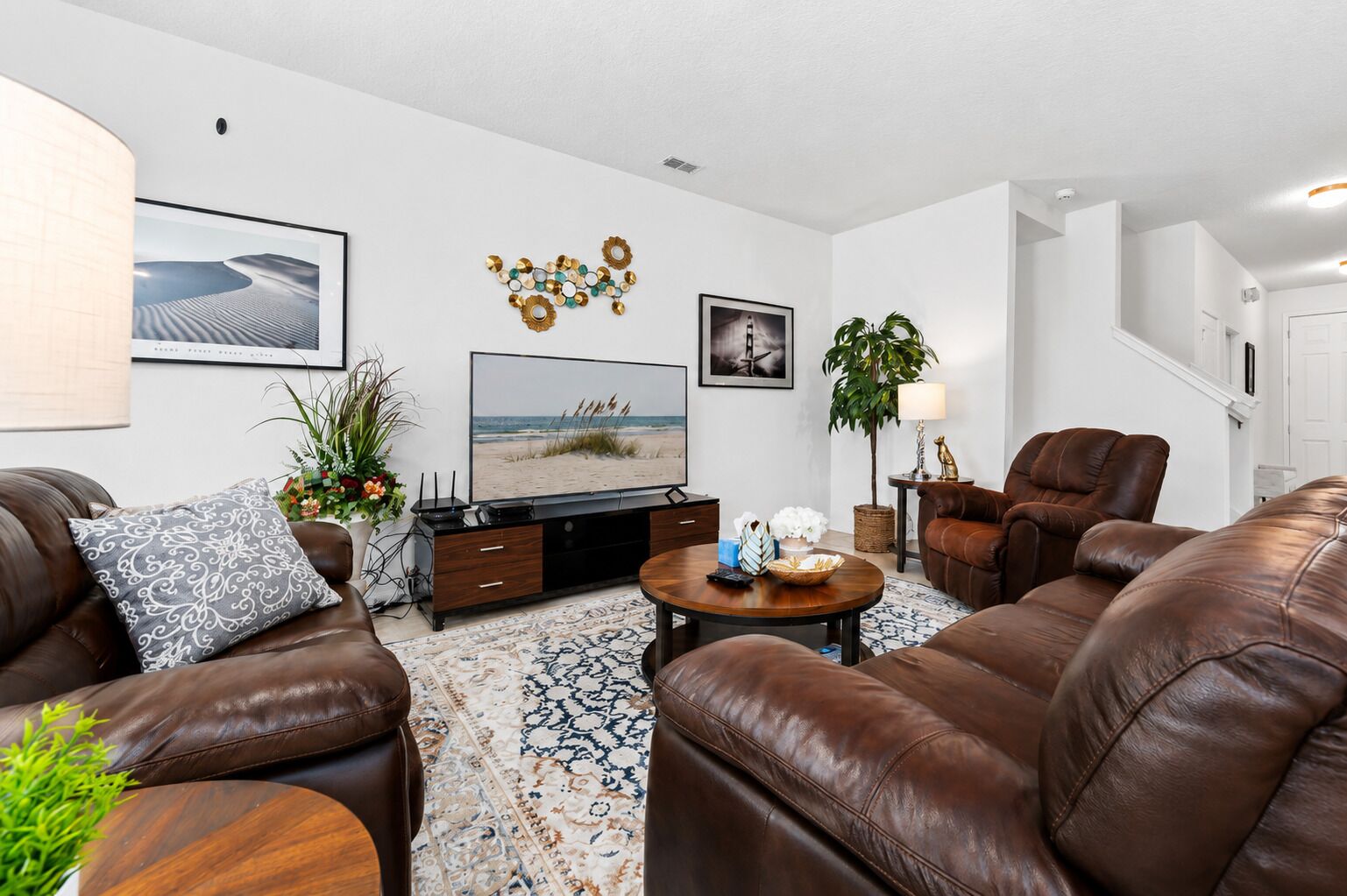 A modern living room with leather sofas, a flat-screen TV, decorative wall art, and a patterned rug.