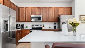 A modern kitchen with stainless steel appliances, wooden cabinets, and a white countertop. - Spacious 10BR resort home with private pool, game room, and room for 25. (Kissimmee)