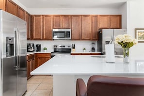 A modern kitchen with stainless steel appliances, wooden cabinets, and a white countertop. - Spacious 10BR resort home with private pool, game room, and room for 25. (Kissimmee)
