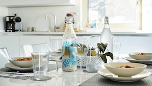 Una mesa de comedor servida con cristalería transparente, una botella decorativa y fuentes de comida.