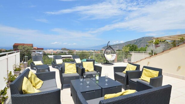 Un área de estar al aire libre con muebles de mimbre y cojines amarillos, con vistas a un paisaje pintoresco.