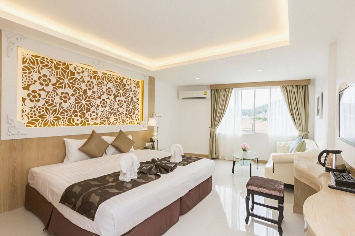 A hotel room with a large bed, a sitting area with a sofa and armchair, a small table, and a view of the outdoors.