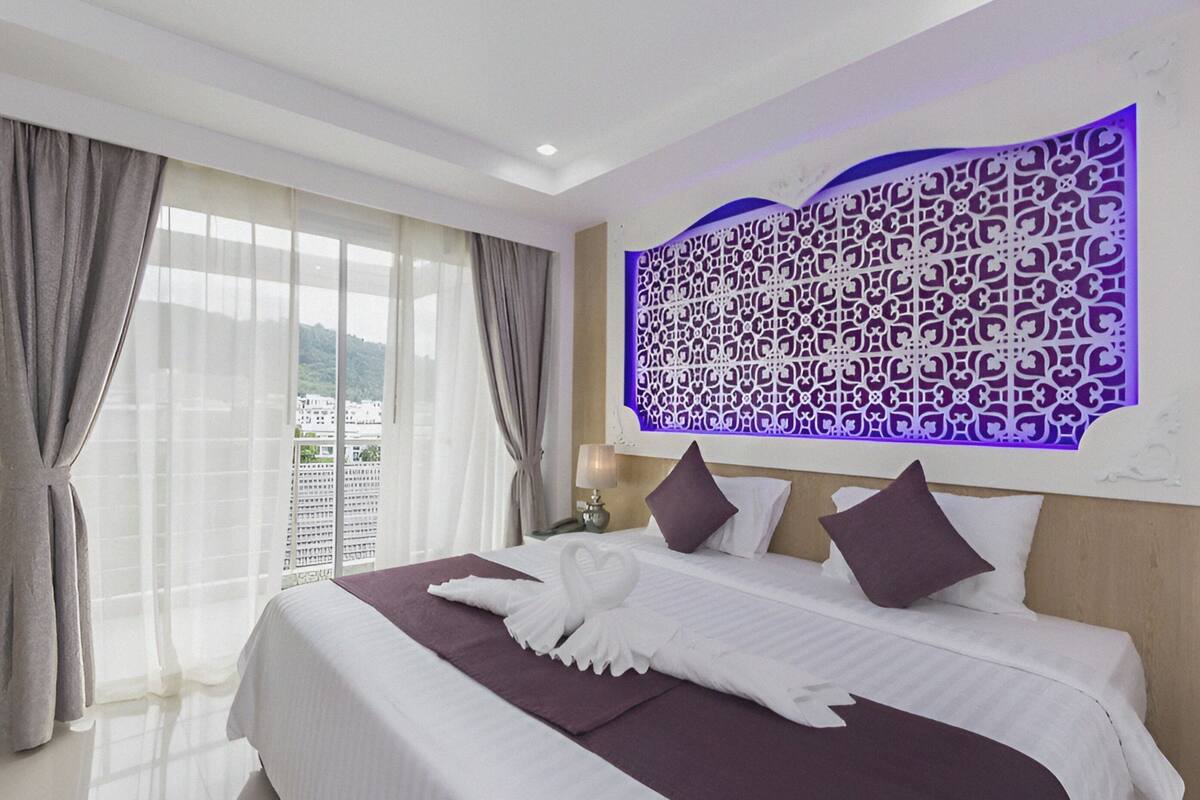 A hotel room with a large bed, a decorative headboard, and a view of the city through the window.