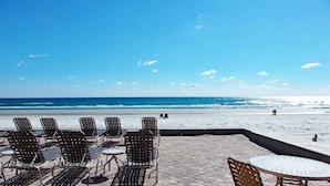Une terrasse au bord de la plage, avec des chaises et des tables en métal, d’où l’on a une vue sur l’océan.