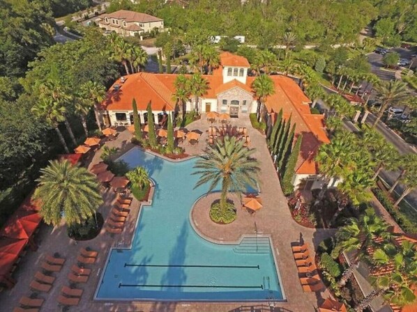 Una piscina amplia rodeada de palmeras y sillas de descanso, con un edificio al fondo.