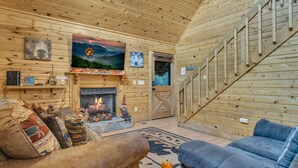 Interior acogedor de una cabaña con chimenea, paredes de madera, un televisor montado y un sofá.
