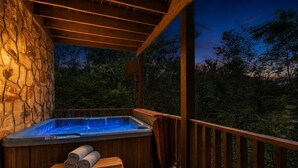Un jacuzzi en una terraza de madera con un muro de piedra de fondo, rodeado de árboles.