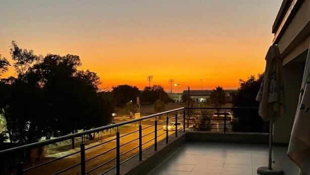 Un balcone con vista su un tramonto su una strada, un pavimento piastrellato e una ringhiera.