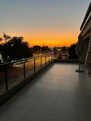 A balcony with a view of a sunset over a road, a tiled floor, and a railing.