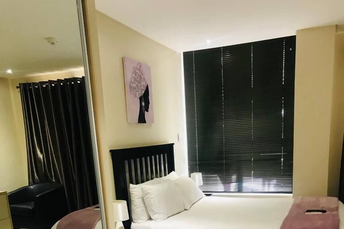 A modern bedroom with a large bed, bedside tables, a mirror, and a window with blinds.