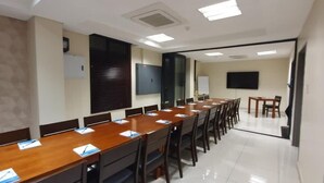 Una sala conferenze con un lungo tavolo, sedie, una lavagna e uno schermo per proiettore.