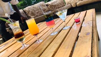 Una mesa de madera con cuatro bebidas encima, un sofá al fondo y una persona con camisa blanca.