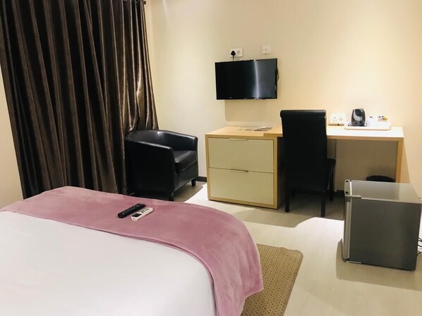 A hotel room with a bed, a desk, a chair, a television, and a refrigerator.