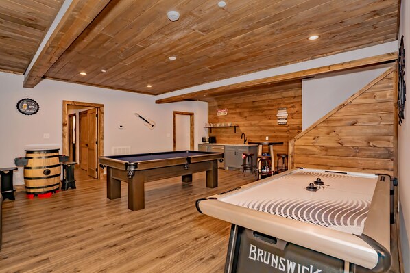 Una sala con suelo de madera, mesa de billar, barra de cerveza y futbolín.