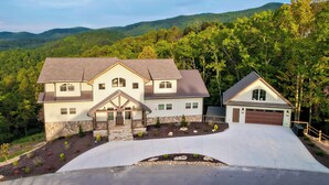 A two-story house with a garage, surrounded by a landscaped garden and a driveway. - A Piece Of Perfect: Pool, Mtn Views, Home Theater, Game Room, Hot Tub, Wifi (Sevierville)